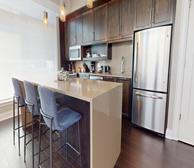 The Avery - Dartmouth short-term furnished apartment kitchen with dark brown wood cabinets, beige island, and blue bar stools - Premiere Suites