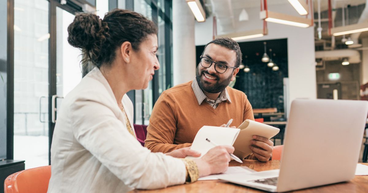 Two employees having a conversation at a desk in a work environment